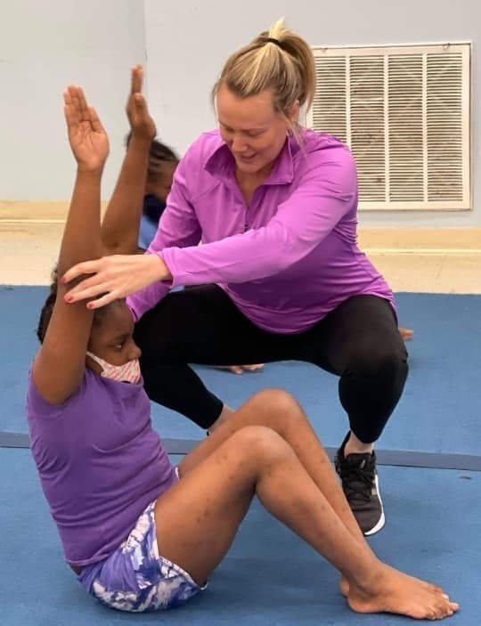 Instructor helping student hold arms up in a class